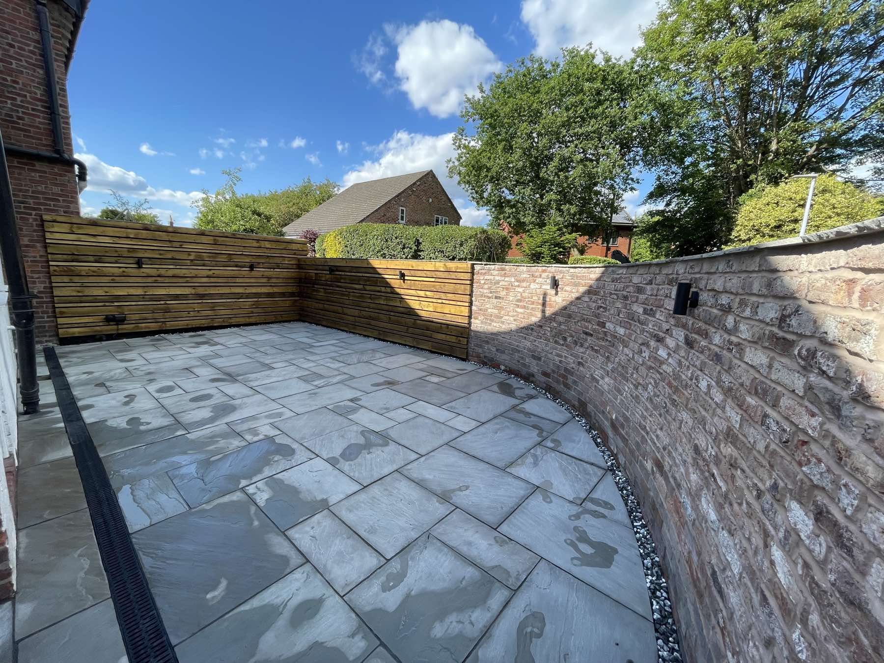 Natural stone patio with a curved brick wall and slatted fence