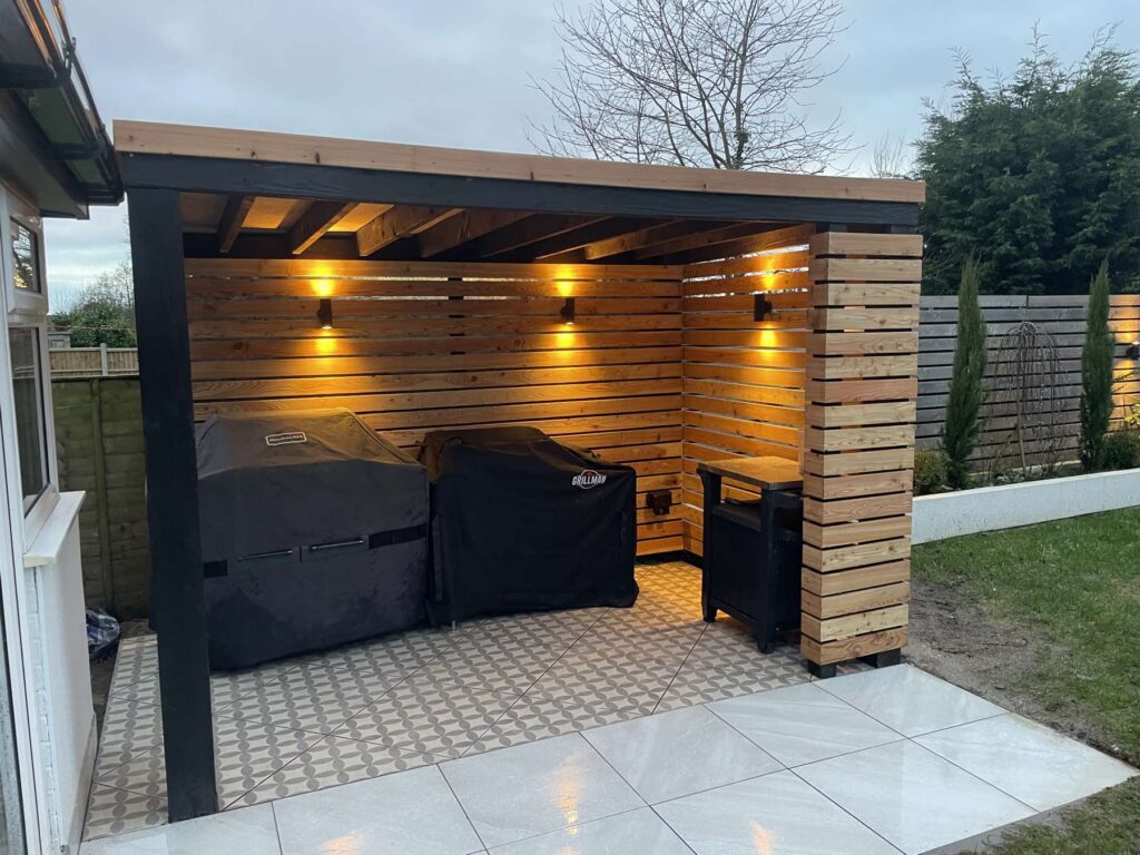 Timber outdoor kitchen shelter with wall lights and patterned tiles