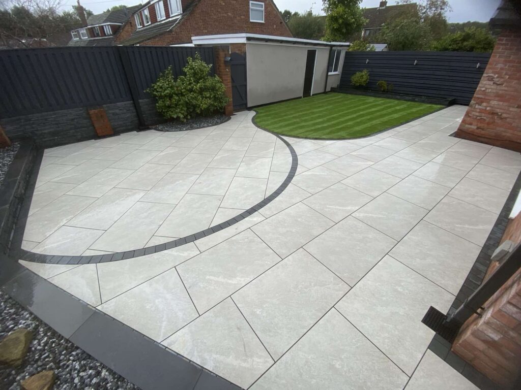 Light grey porcelain patio with a curved dark border and a striped lawn