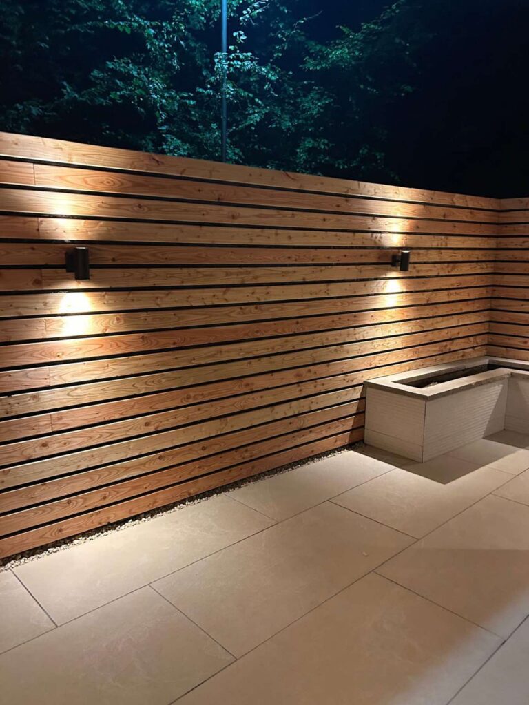 Slatted timber fence with wall lights above a porcelain patio at night