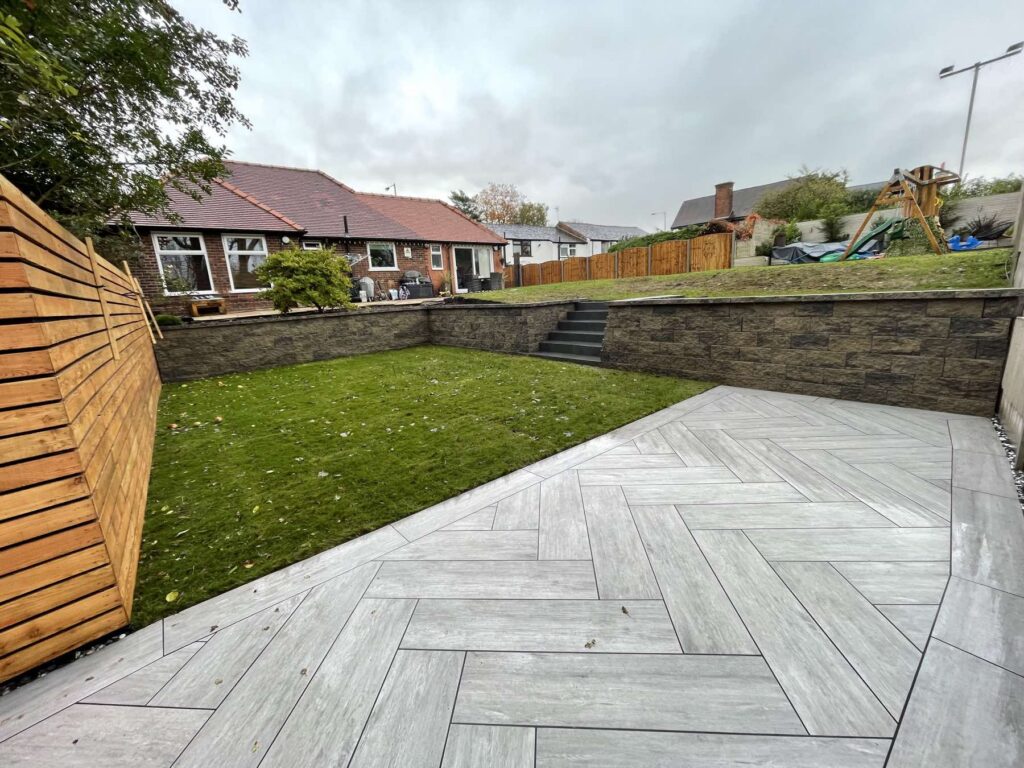 Wood-effect porcelain in herringbone with a retaining wall and lawn